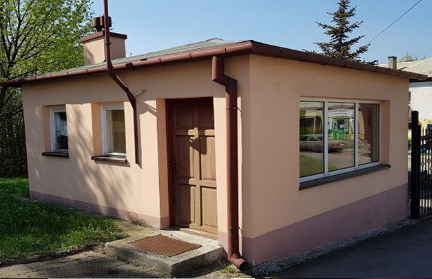 Niewielki budynek z różowym tynkiem, drzwiami i trzema oknami.